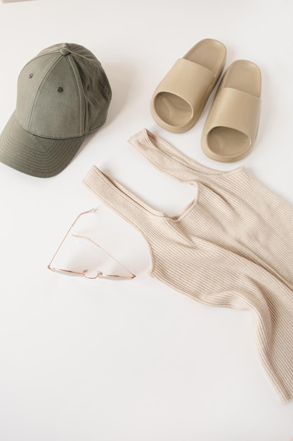 Minimal fashion concept with sport women's clothes on white background Beige slippers top sunglasses cap