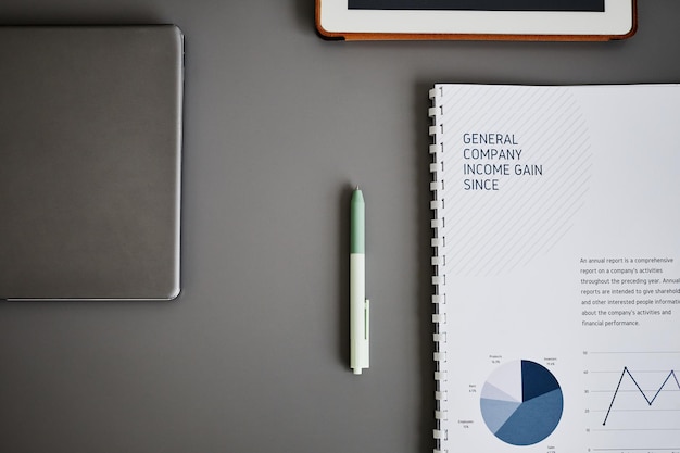 Minimal flat lay of business tools on grey desk focus on pen and finance notebook