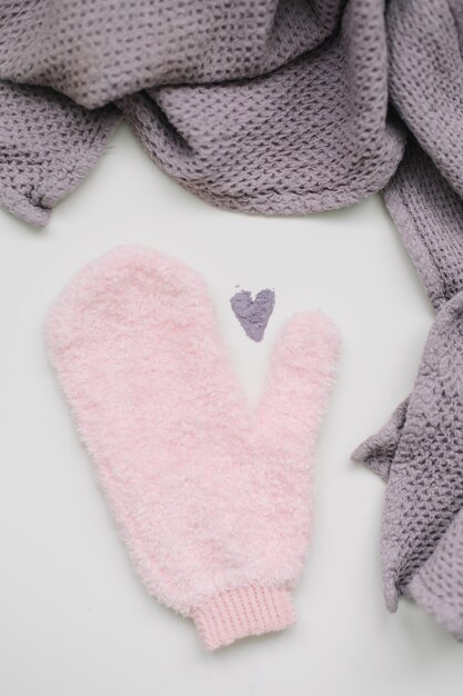 Minimal flat lay composition of massage mitten washcloth and a heart made of violet powder on a whit...