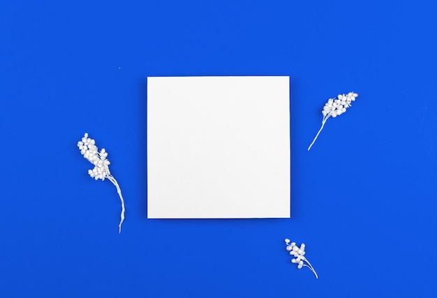 Minimal flat lay concept with blank white card, mockup floral background on a blue paper with dried flowers