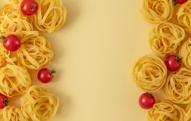 写真 最小限のフードパターンのタリアテッレとトマト、明るい黄色のパステルカラーの背景。ポップアートスタイルの伝統的なイタリアンパスタ。パスタとトマト、イタリア料理のコンセプト。上面図、フラットレイ、コピースペース