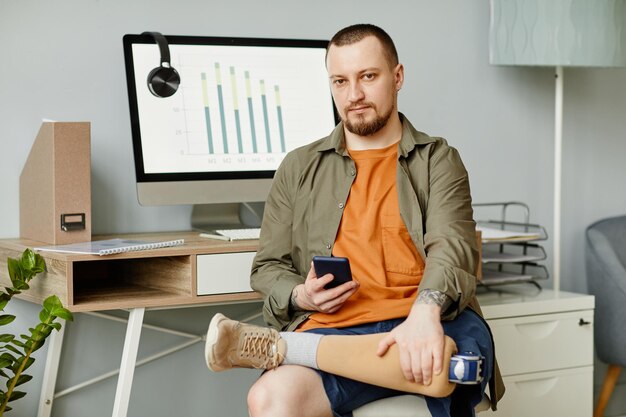 Minimal front view portrait of adult man with prosthetic leg at\
workplace looking at camera