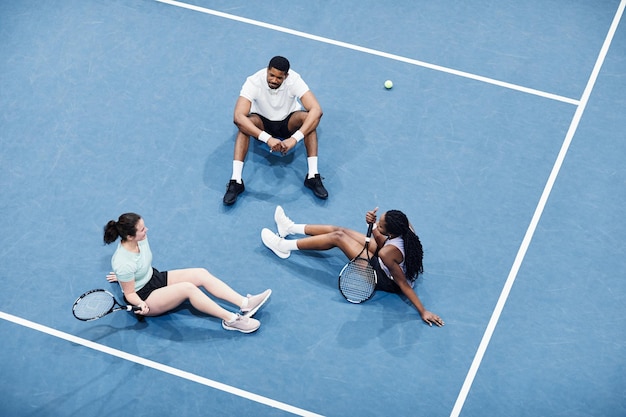 Minimal high angle at group of people relaxing at indoor tennis court and sitting on graphic blue fl