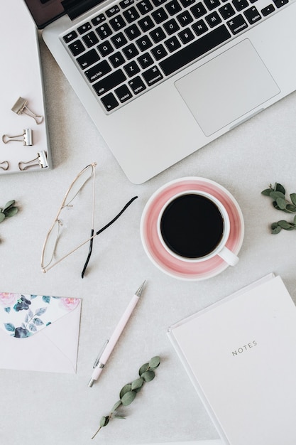 Minimal home office desk workspace with laptop, coffee, notebook, eucalyptus, envelope