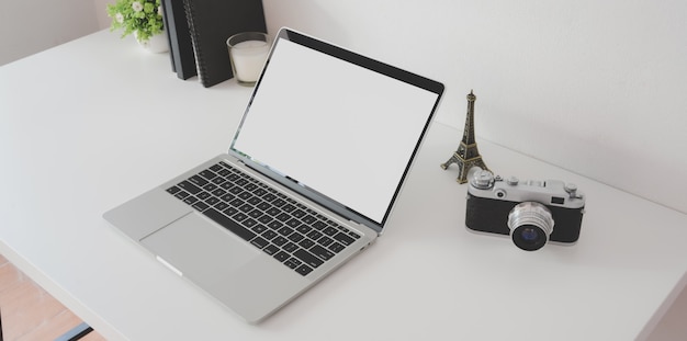 Foto area di lavoro minima del fotografo con il computer portatile aperto dello schermo in bianco con la macchina fotografica d'annata