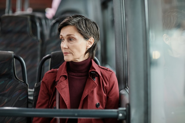 Photo minimal portrait of mature woman sitting in bus and looking away while traveling by public transport...