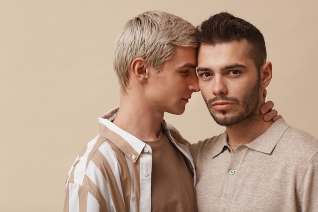 Фото Минимальный портрет молодой гей-пары, обнимающейся во время позирования на нейтральном бежевом фоне в студии, копией пространства