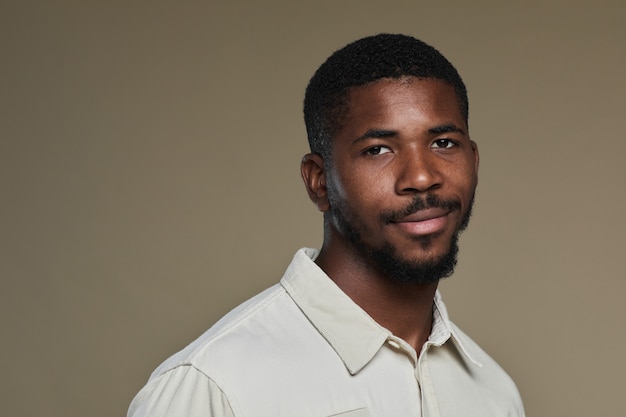 Minimal portrait of young africanamerican man looking at camera and smiling while posing against neu...