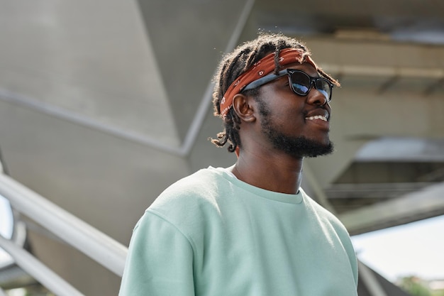 Minimal portrait of young black man wearing street style clothes looking to side and smiling in urba