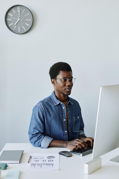 Minimal portrait of young black professional at workplace in\
office using pc computer with analog cl