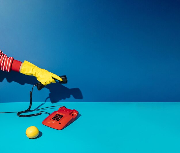 赤いビンテージ電話に答える黄色のクリーニング グローブで手で最小限のレトロなコンセプト