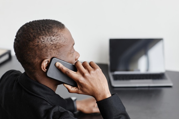 Минимальный снимок афроамериканца, говорящего по смартфону в черно-белом внутреннем копировальном пространстве
