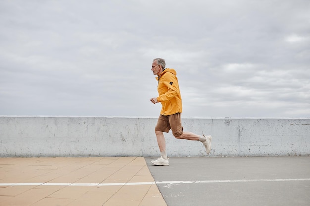 Minimal side view portrait of handsome mature man running by river against grey sky