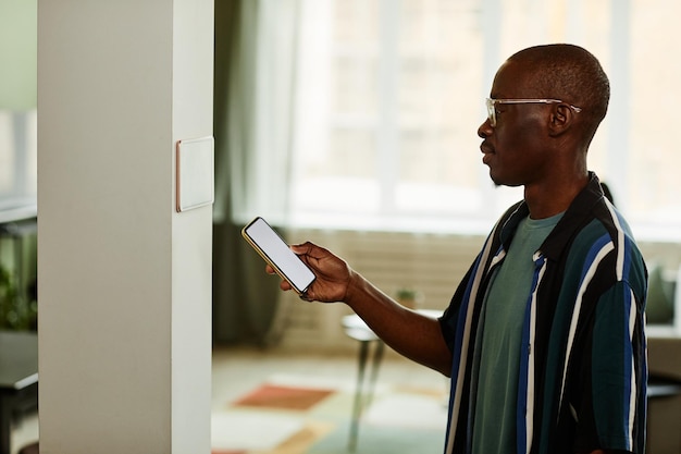 Minimal side view portrait of modern african american man using\
phone while connecting to smart home system