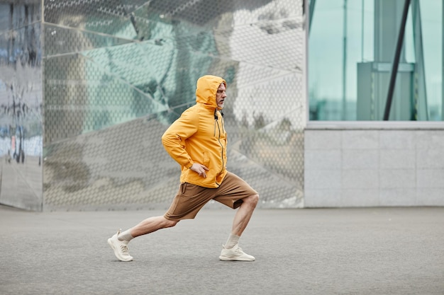 Minimal side view portrait of sportive mature man stretching outdoors in urban city setting and wear