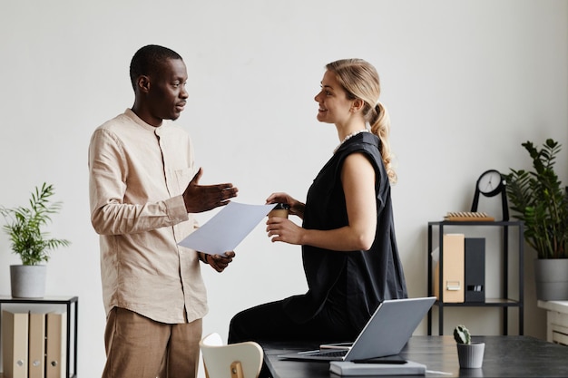 Minimal side view portrait of two business people discussing project by desk in office copy space