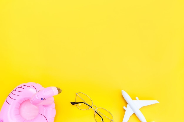 Minimal simple flat lay with plane sunglasses and Inflatable flamingo isolated on yellow