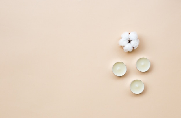 Minimal spa treatment composition. White aroma candles, cotton boll on light Beige background. Flat lay, copy space, top view.