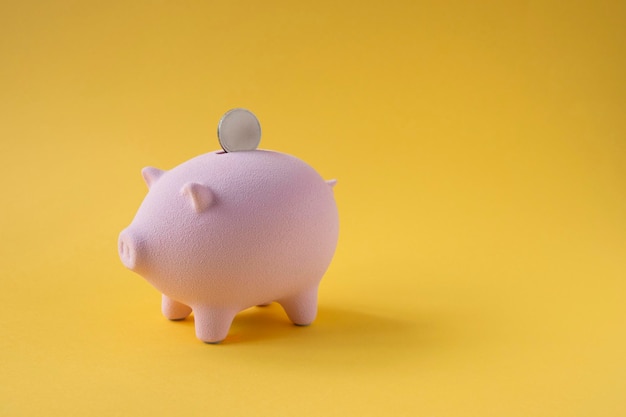 Minimal style piggy bank with coin on yellow background