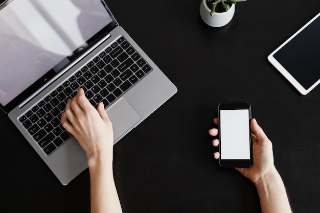 Minimal top view background of female hands holding smartphone with blank screen while working at bl...