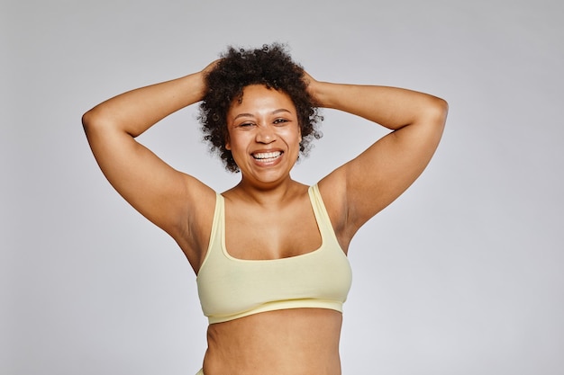 Minimal waist up portrait of carefree black woman wearing underwear and laughing happily against gre