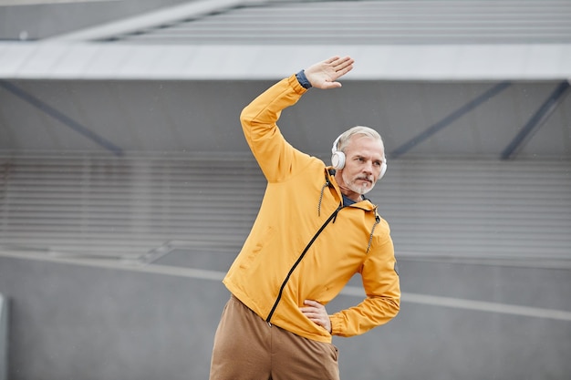 Фото Минимальный поясной портрет спортивного зрелого мужчины, растянувшегося на улице с наушниками в городском городе
