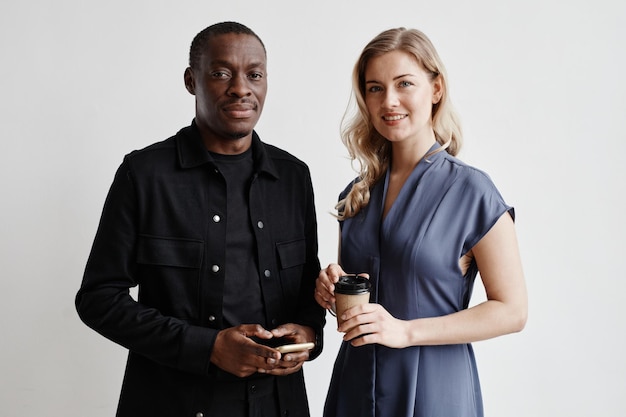 Minimal waist up portrait of two modern business people looking at camera while standing by white wa...