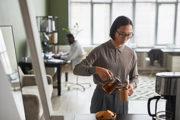 Photo minimal waist up portrait of young asian man making coffee in office and wearing grey copy space