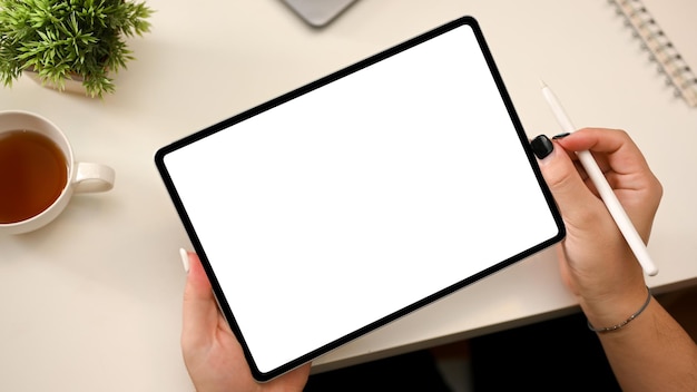 Minimal white office desk with a female holding portable tablet empty screen mockup with stylus pen