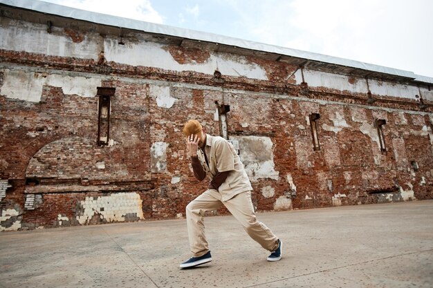 Minimal wide angle shot of young man dancing hiphop outdoors in\
shabby urban setting and hiding face