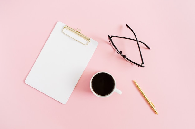 Minimal women home office desktop with clipboard, pen, coffee mug and glasses on pink