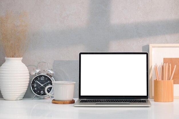 Minimal workplace with laptop computer coffee cup pencil holder and picture frame on white table