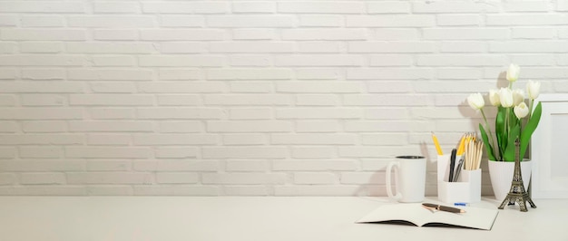 Minimal workplace with potted plant pencil holder and books on\
white table against brick wall copy space for your text