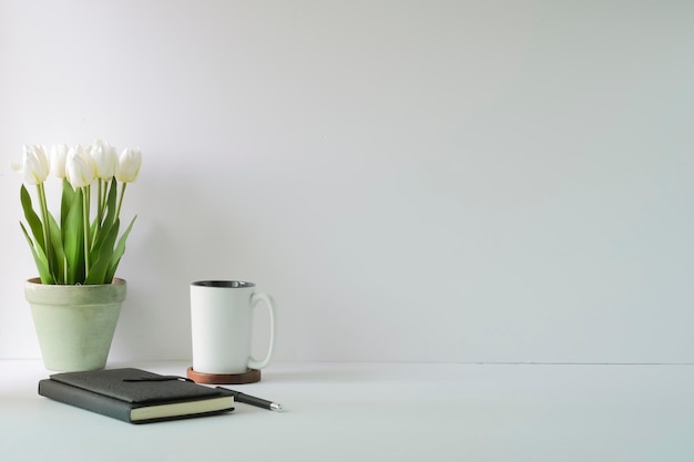 Minimal workplace with white tulips bouquet in a pot coffee cup and notebook Copy space for advertise text or information content