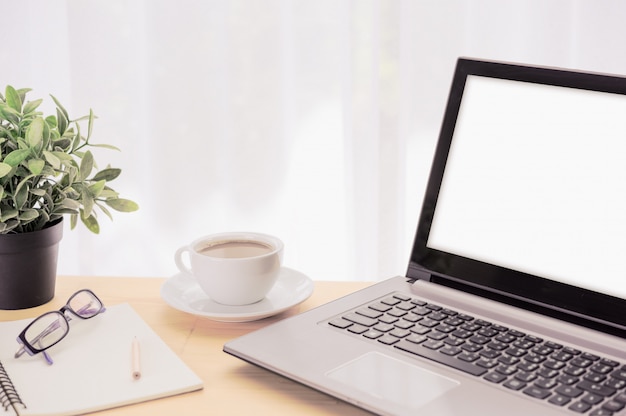 Минимальное рабочее пространство, компьютер ноутбук, чашка кофе, зеленый цветочный горшок, очки и блокнот на деревянный стол