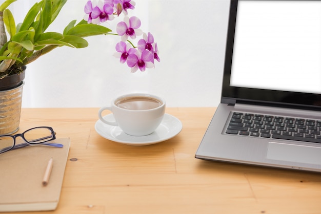 Area di lavoro, computer portatile, tazza di caffè, fiore dell'orchidea e taccuino minimi sulla tavola di legno