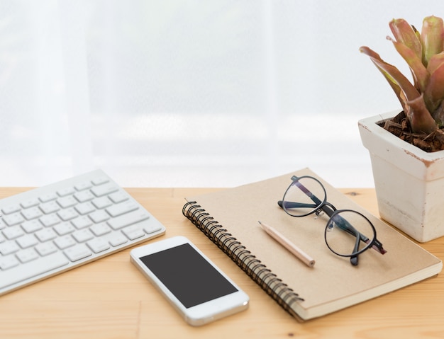 Minimal workspace, computer, smartphone, notebook, pencil and eyeglasses on wood table