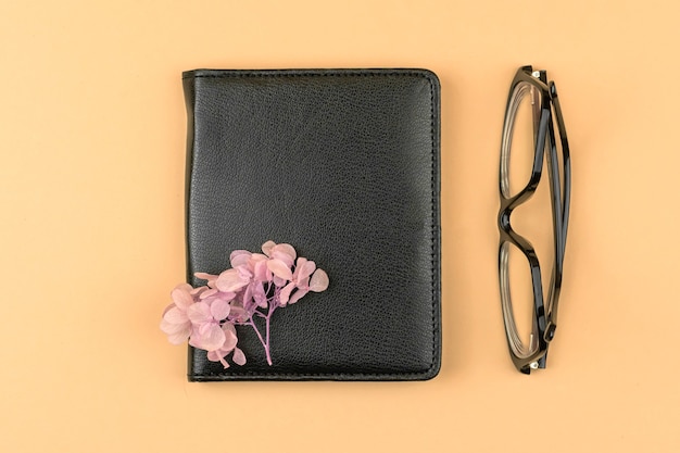 Minimal workspace concept with black leather notebook, pink dried flower and glasses, top view composition photo