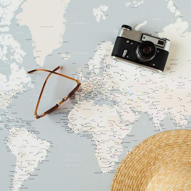 Minimal world map with pins, retro camera, sunglasses, straw hat. Flat lay vacation travel planning