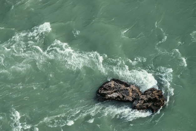 Foto minimale aardachtergrond van turkoois bergrivierfragment. grote kei in donkergroene berg rivier stroom close-up. natuurlijke achtergrond met grote steen in waterstroom. aardtextuur van water met rots.