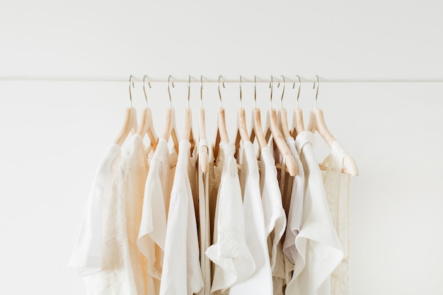 Minimale mode kleding concept. Witte vrouwelijke blouses en t-shirts op hanger op wit.