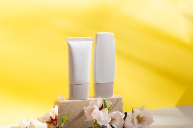 Minimale moderne productweergave voor cosmetische buizen op grijze en gele achtergrond met podium en amandelboomtakje met bloemen