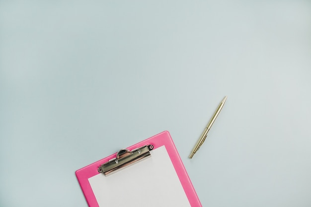 Minimale plat leggen, bovenaanzicht van klembord en gouden pen op pastelblauw oppervlak