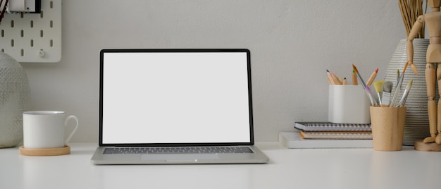 Minimale werktafel met leeg scherm laptop, beker, tekengereedschappen en decoraties op witte tafel