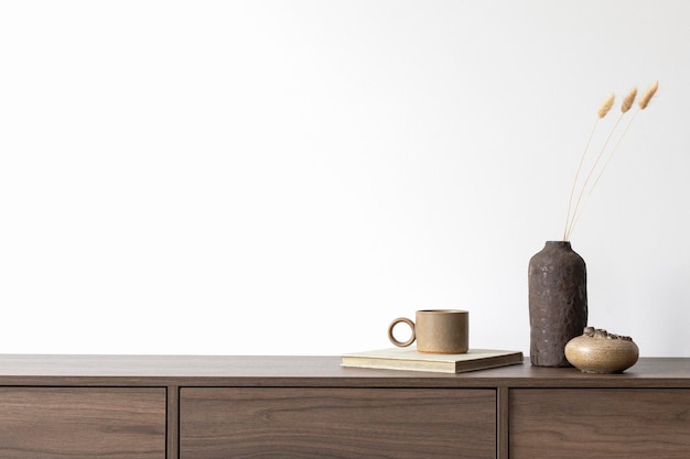 Минималистичная композиция интерьера современной гостиной с коричневым комодом, вазами и личными аксессуарами. Белая стена. Скопируйте пространство. Шаблон.
