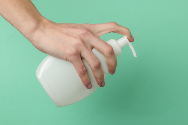 Minimalism beauty concept. Female hand hold a bottle of cream on blue background