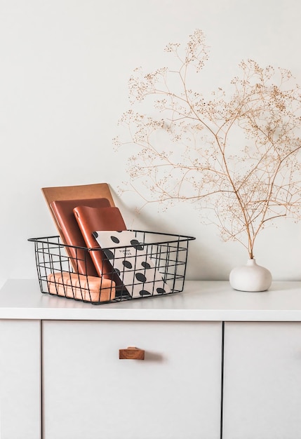 Minimalism interior black metal basket with notebooks and natural decor on a white table in the living room