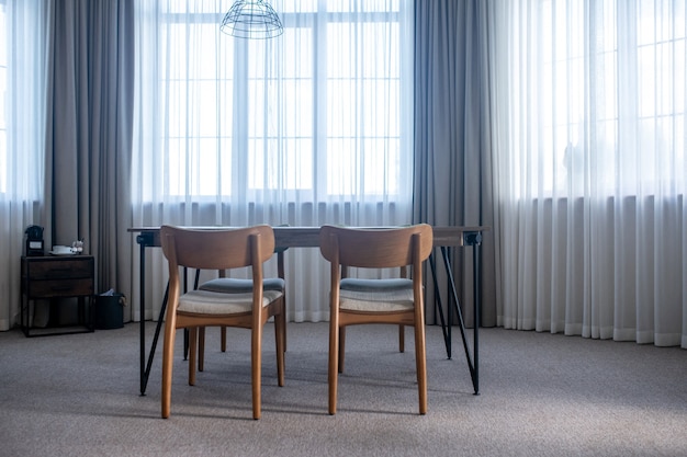 Photo minimalism. table with chairs on carpet in center of room with large windows with curtains during day