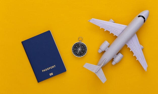 Minimalism travel, adventure flat lay. Compass and air plane, passport on yellow background. Top view