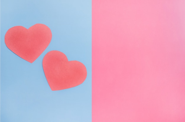 Minimalisme achtergrond voor Valentijnsdag, twee rode harten op een roze en blauwe achtergrond met kopie ruimte.